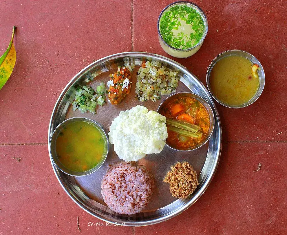 A traditional South Indian thali at Mango Mulch — red rice, dal, sambar, and vegetable curries on a steel plate