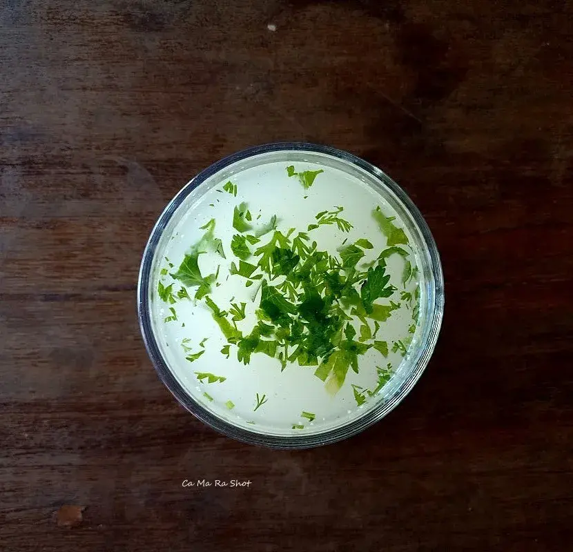 A glass of buttermilk topped with fresh coriander leaves