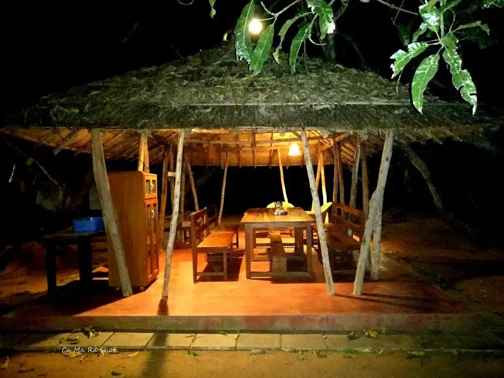 The open-air thatched dining pavilion under the mango trees, lit by a single lamp at night