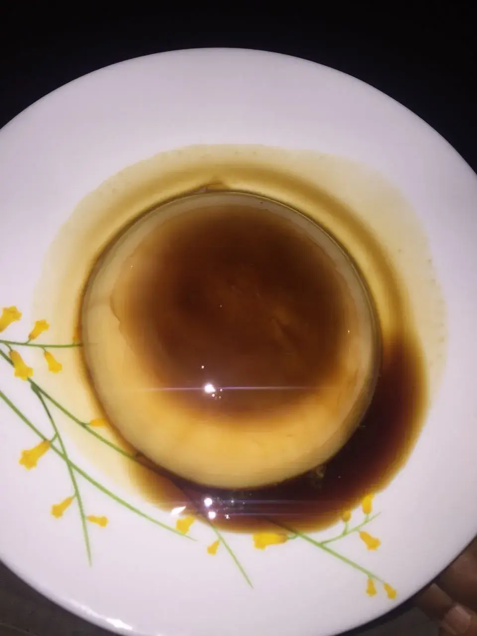 Vegetarian caramel custard plated with a sprig of yellow flowers